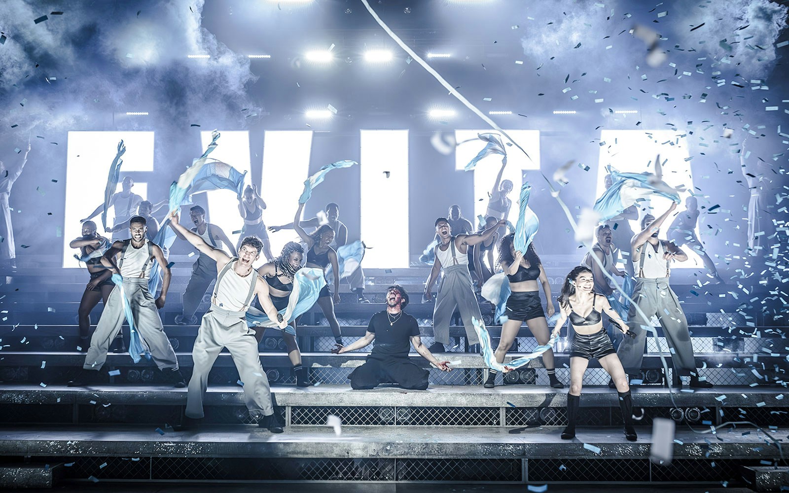 Performers on stage during Evita musical with blue and white flags.