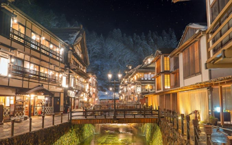 Ginzan Onsen village at night with traditional wooden buildings and a lit bridge in Japan.