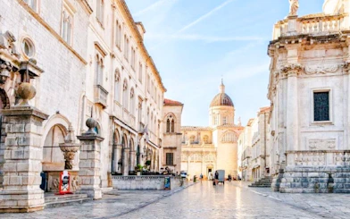 Placa street in Dubrovnik's Old Town with historic buildings and a distant dome.