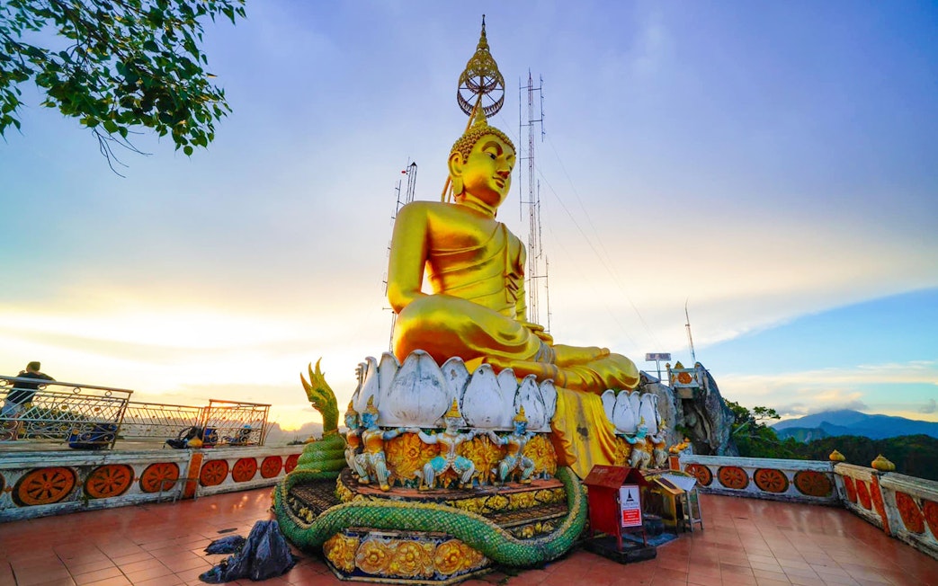 Buddha statue at Tiger Cave Temple, Krabi, with scenic mountain view.