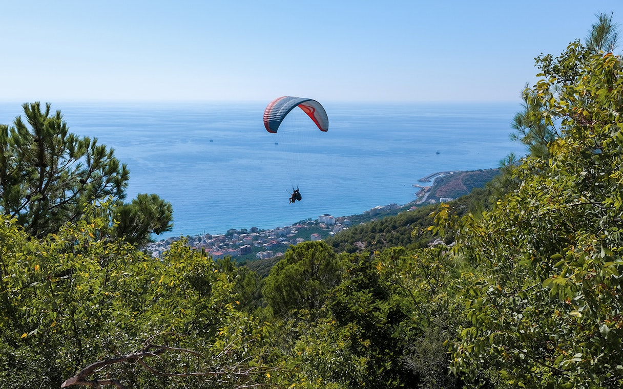 Paraglider soaring over Alanya coastline with sea and forest views.