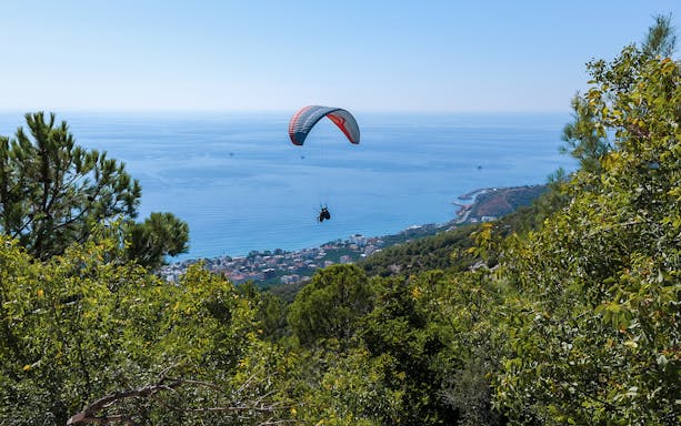 Paraglider soaring over Alanya coastline with sea and forest views.