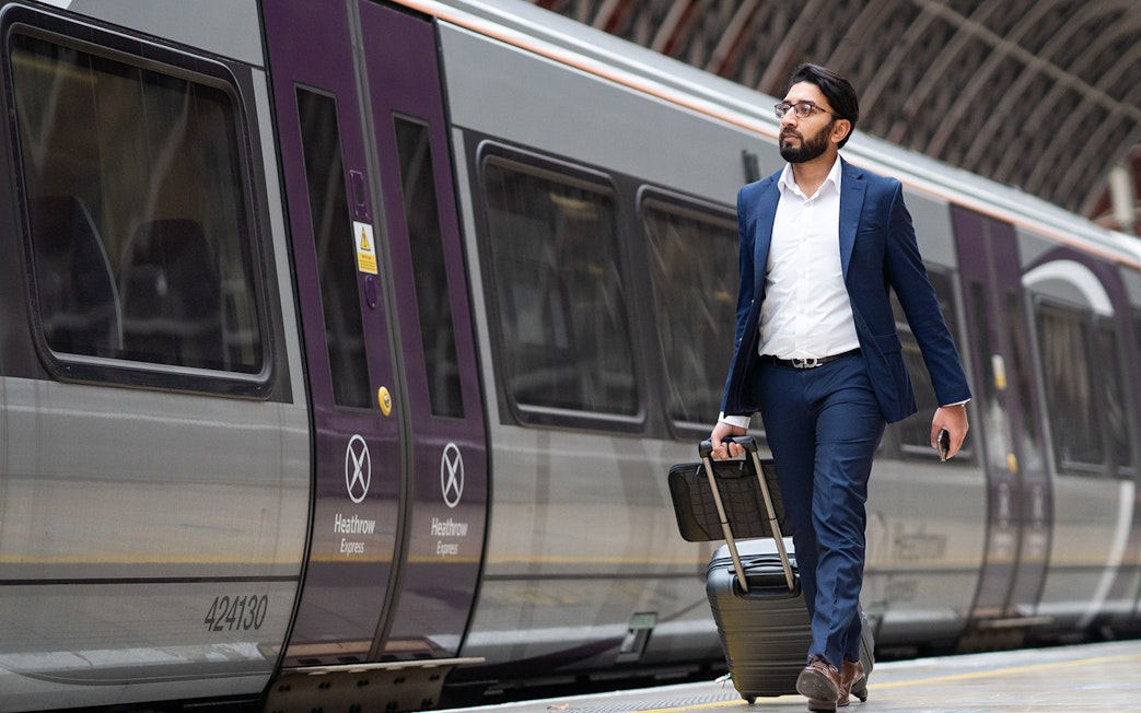 Passenger with luggage walking beside Heathrow Express train at station.
