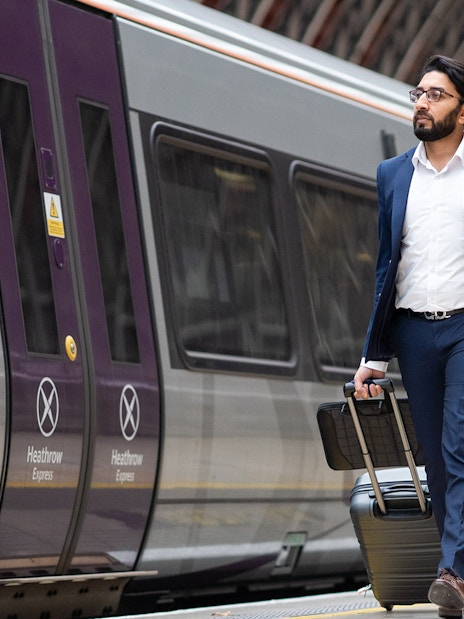 Passenger with luggage walking beside Heathrow Express train at station.