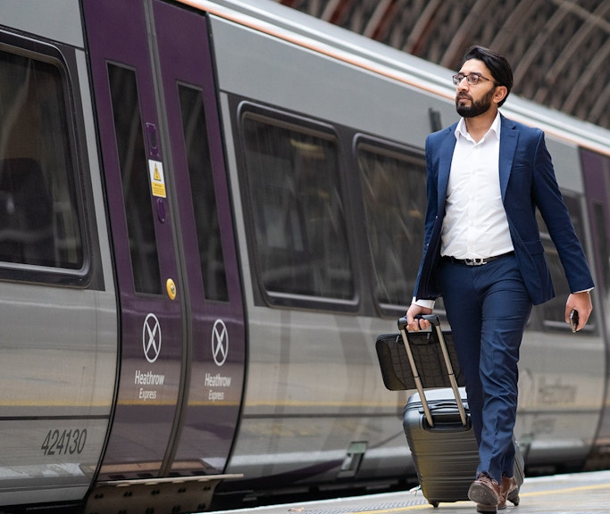 Passenger with luggage walking beside Heathrow Express train at station.