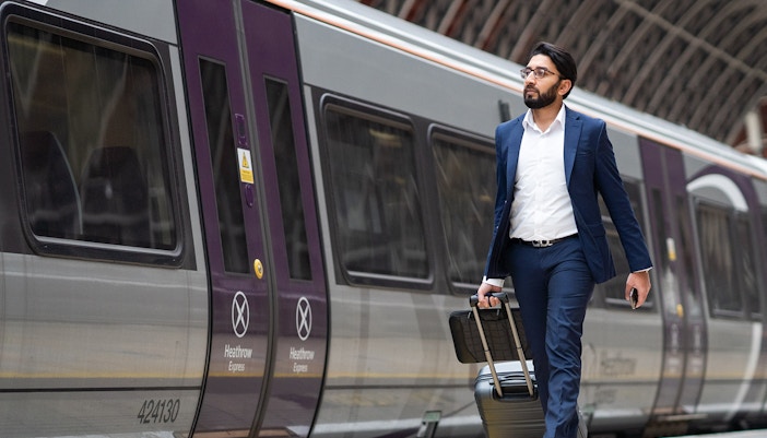 Passenger with luggage walking beside Heathrow Express train at station.