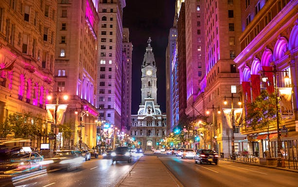 Philadelphia City Hall illuminated at night with vibrant street lights.
