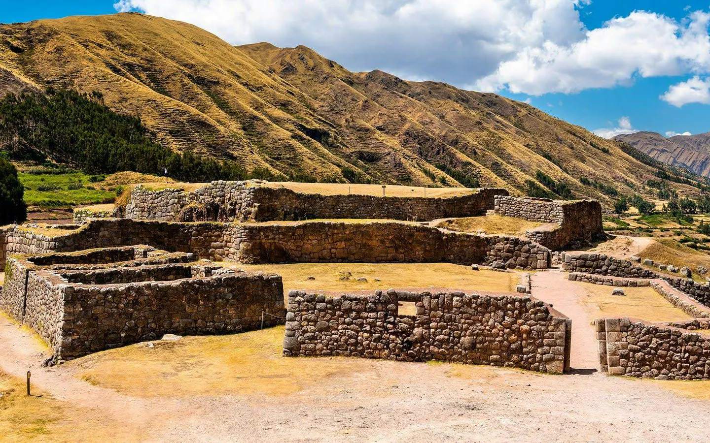 Ancient stone ruins at an archaeological site near Cusco, Peru, with mountainous backdrop.