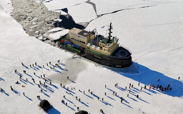 Icebreaker Arktis navigating frozen sea with tourists walking on ice, Kemi.