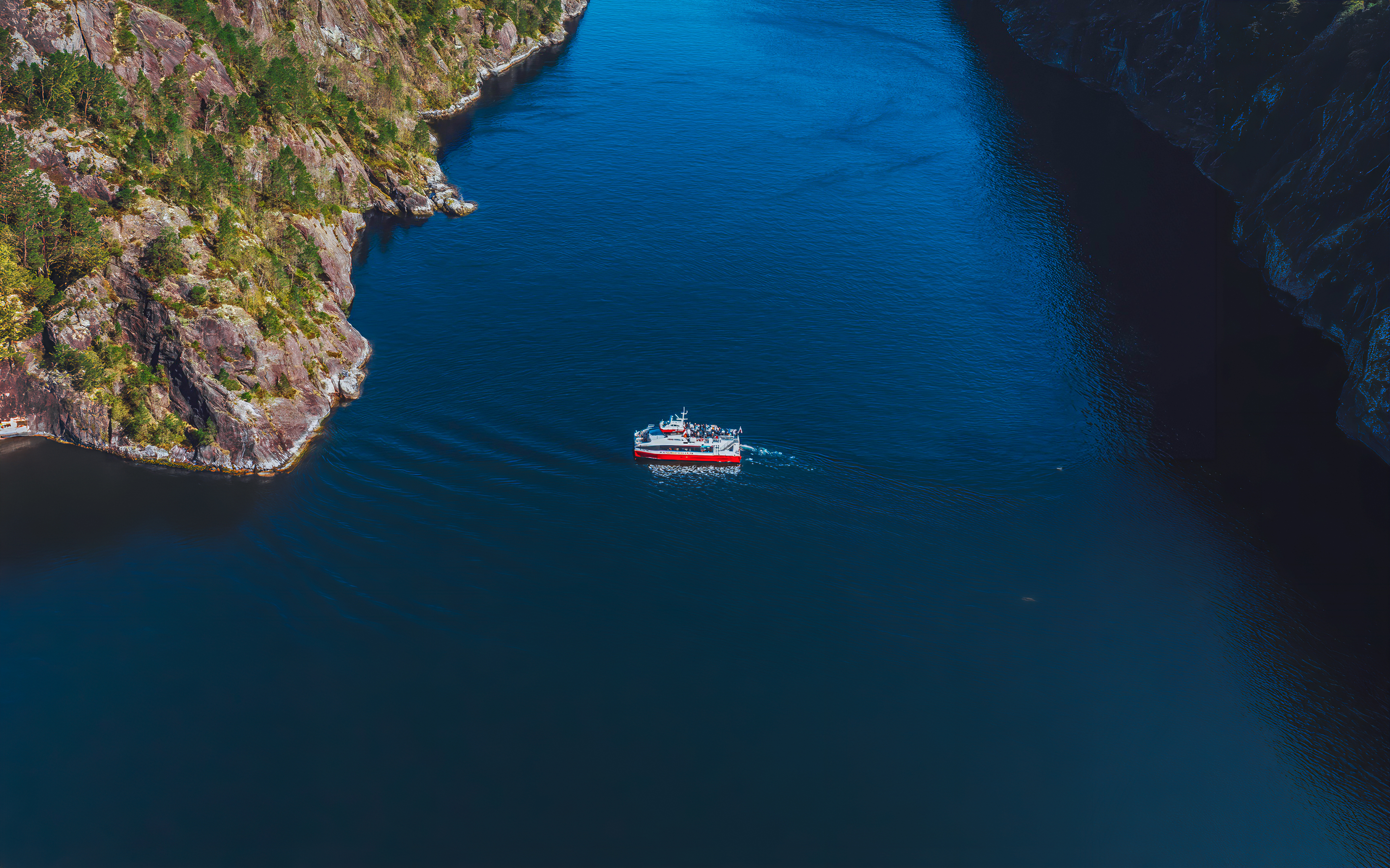 Cruise boat navigating Mostraumen Fjord near Bergen, surrounded by steep cliffs.