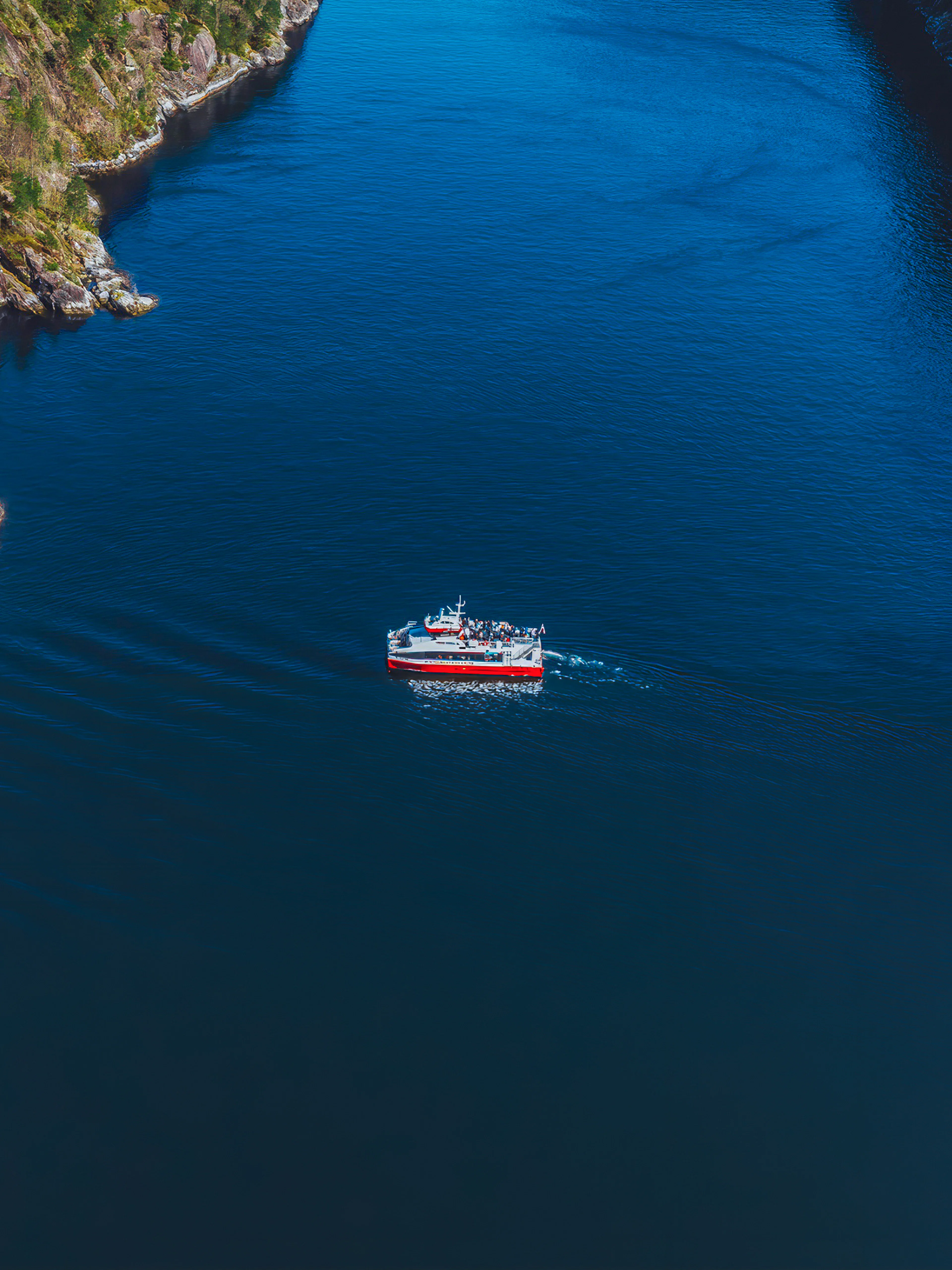 Cruise boat navigating Mostraumen Fjord near Bergen, surrounded by steep cliffs.
