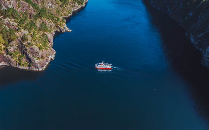 Cruise boat navigating Mostraumen Fjord near Bergen, surrounded by steep cliffs.