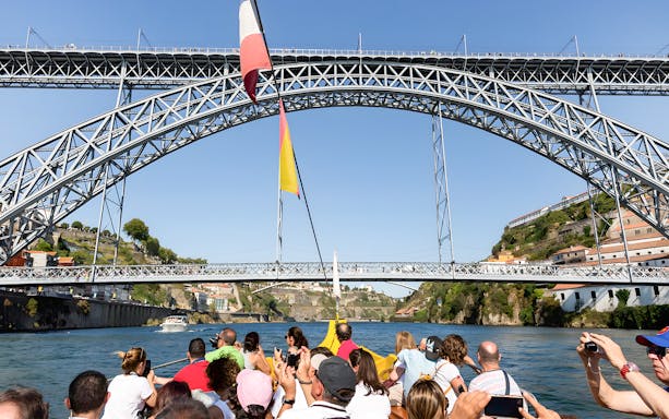 Passengers on Douro River cruise viewing Porto's iconic bridges.