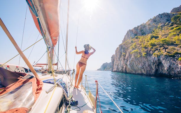 Yacht sailing near rocky cliffs in Hvar with a person enjoying the view.