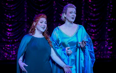 Two performers singing on stage in a scene from My Fair Lady.