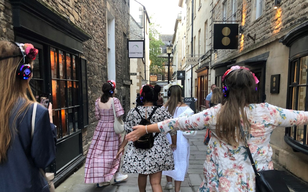 Tour group in period costumes with headphones walking through Bath's historic streets.