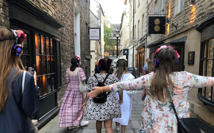 Tour group in period costumes with headphones walking through Bath's historic streets.