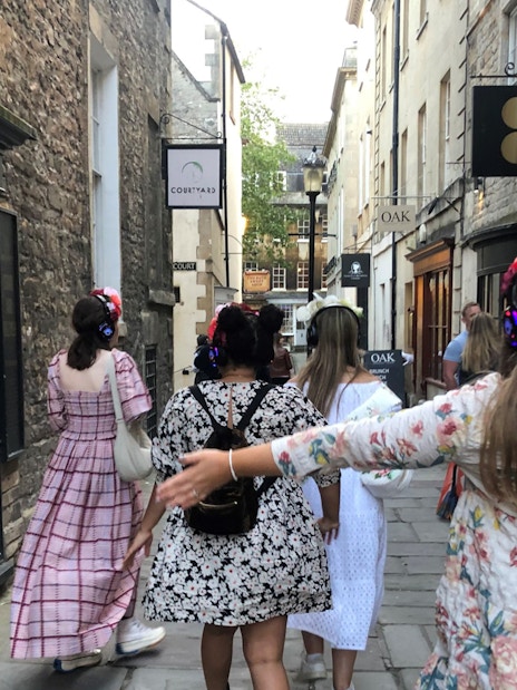 Tour group in period costumes with headphones walking through Bath's historic streets.