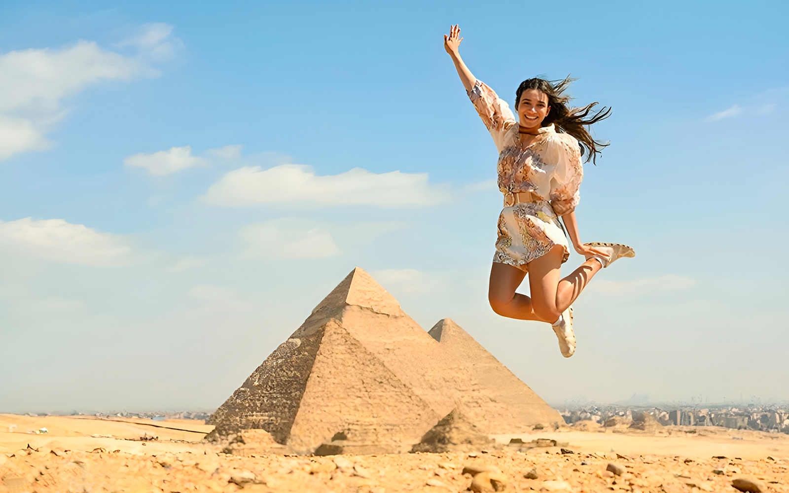 Person jumping in front of the Pyramids of Giza, Cairo, during a tour.