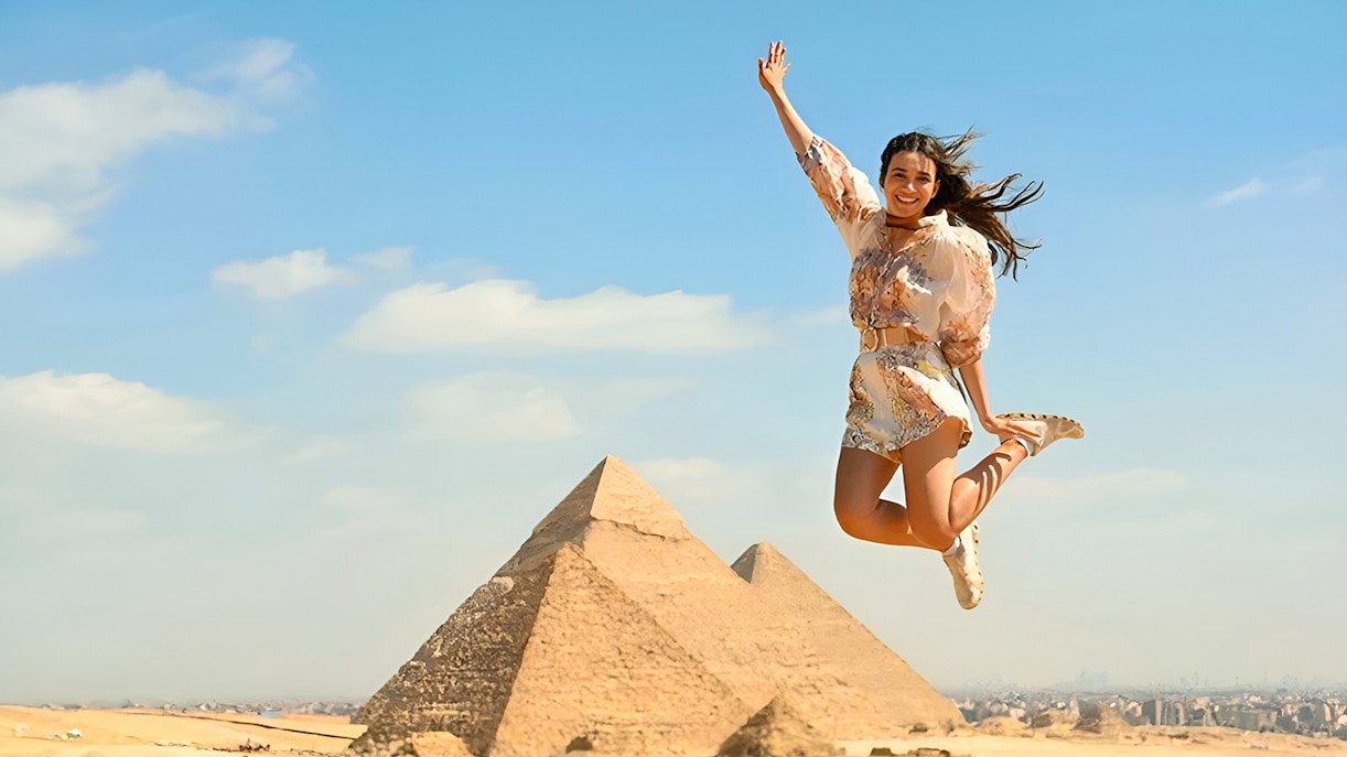 Person jumping in front of the Pyramids of Giza, Cairo, during a tour.