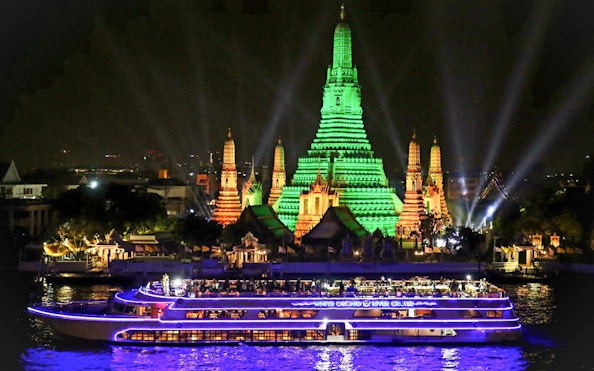 Cruise boat on Chao Phraya River with Wat Arun illuminated at night, Bangkok.