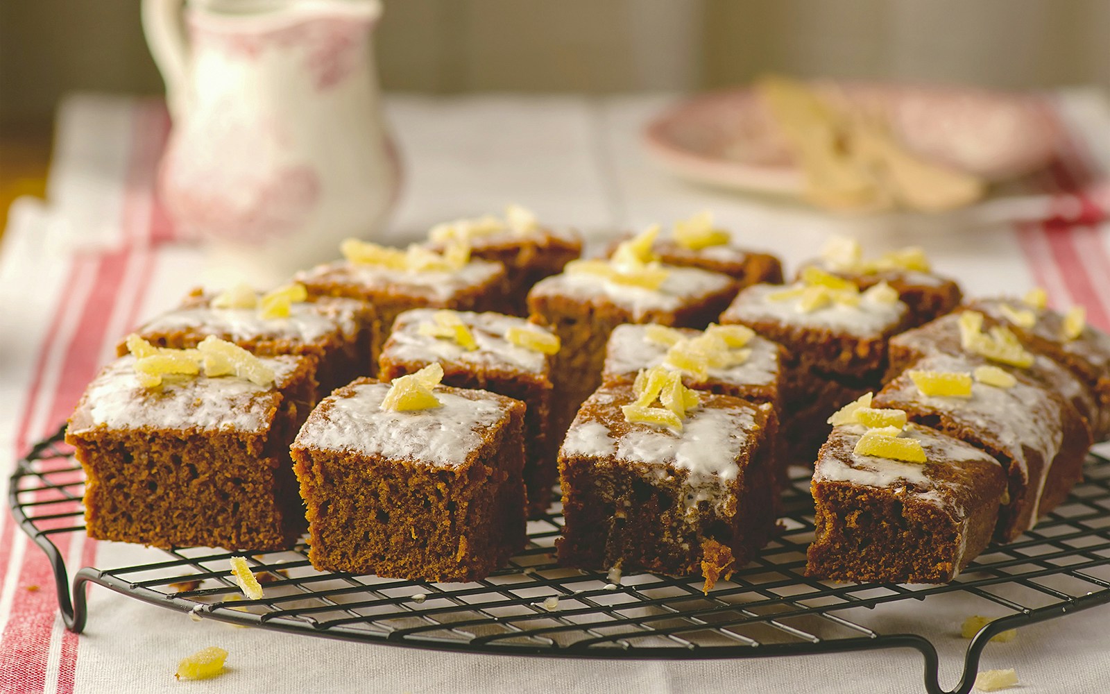 Slices of ginger parkin with icing and candied ginger on a cooling rack.