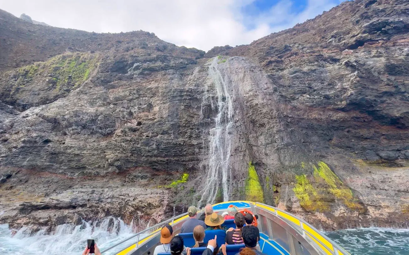 Tourists on a raft approaching a waterfall on the NaPali Coast, Hawaii.