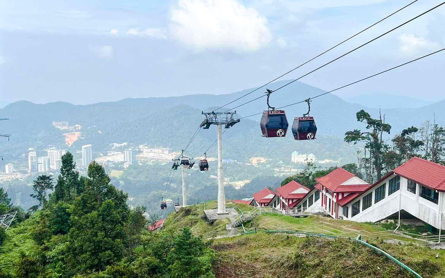Aerial view of Genting Highlands cable cars over lush hills and buildings.