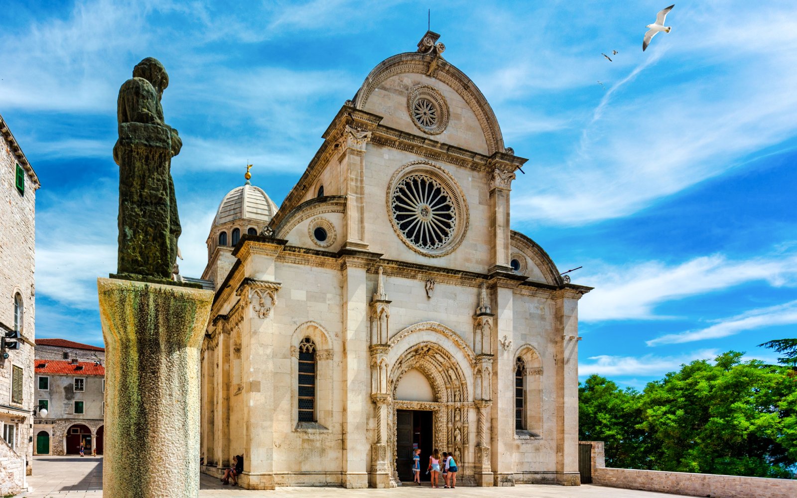 Cathedral of St. James in Šibenik with visitors at the entrance and a statue in the foreground.