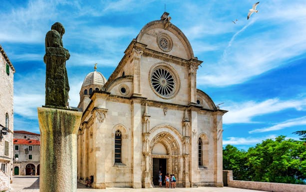Cathedral of St. James in Šibenik with visitors at the entrance and a statue in the foreground.