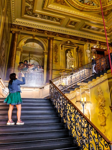 Tourists exploring ornate staircase at Kensington Palace, London.