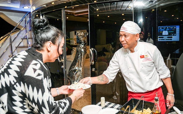 Tourist receiving pasta from chef on Superyacht TriDeck Cruise.