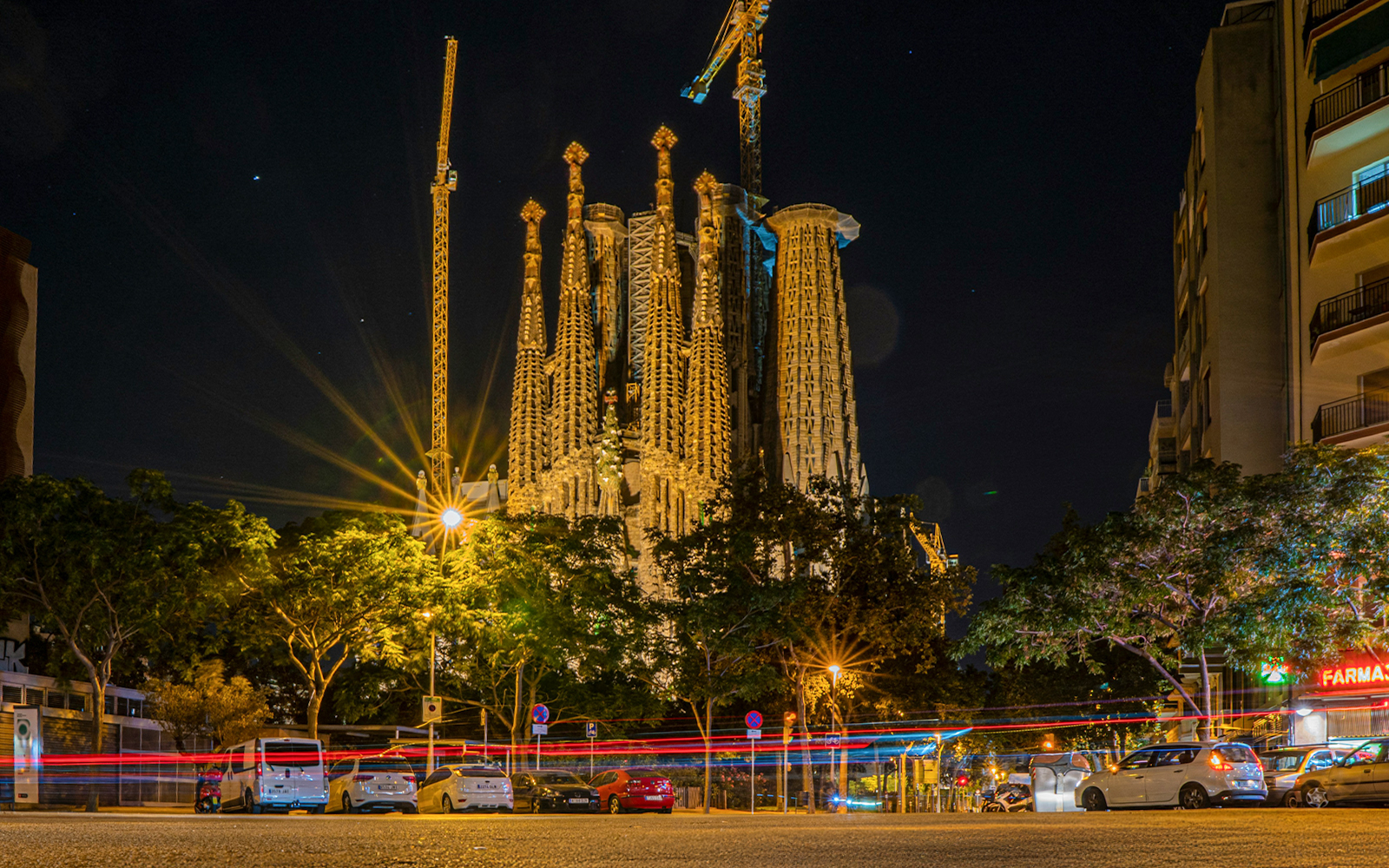 Night view of Sagrada Familia in Barcelona with illuminated spires and surrounding street.