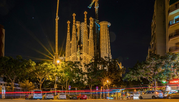 Night view of Sagrada Familia in Barcelona with illuminated spires and surrounding street.