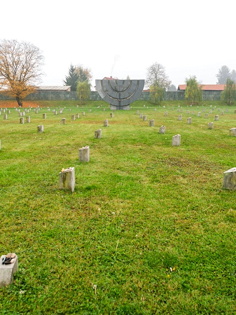 Terezin Concentration Camp memorial field with stone markers and a large menorah sculpture.