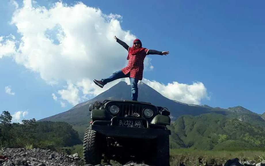 Person standing on Jeep with Mount Merapi in background during sunrise tour, Dubai.