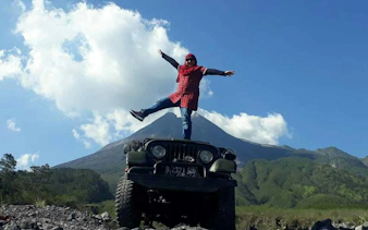 Person standing on Jeep with Mount Merapi in background during sunrise tour, Dubai.