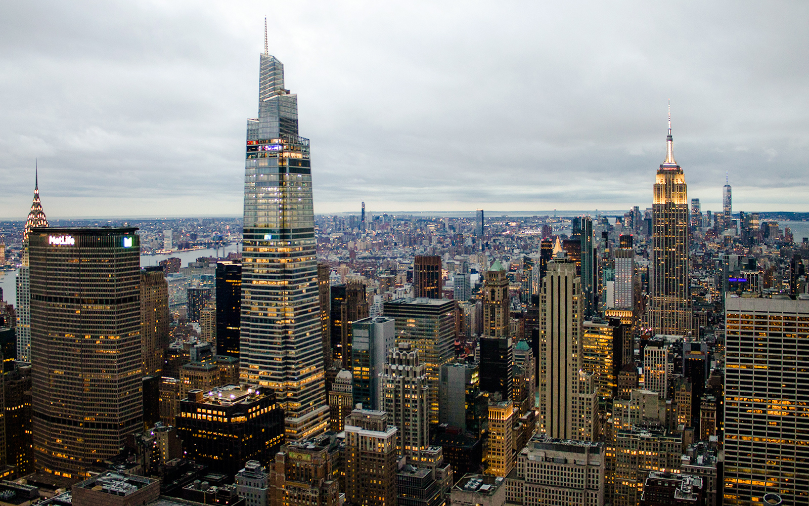 New York City skyline at dusk with Empire State Building and One Vanderbilt illuminated.