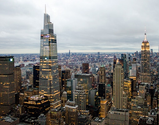 New York City skyline at dusk with Empire State Building and One Vanderbilt illuminated.