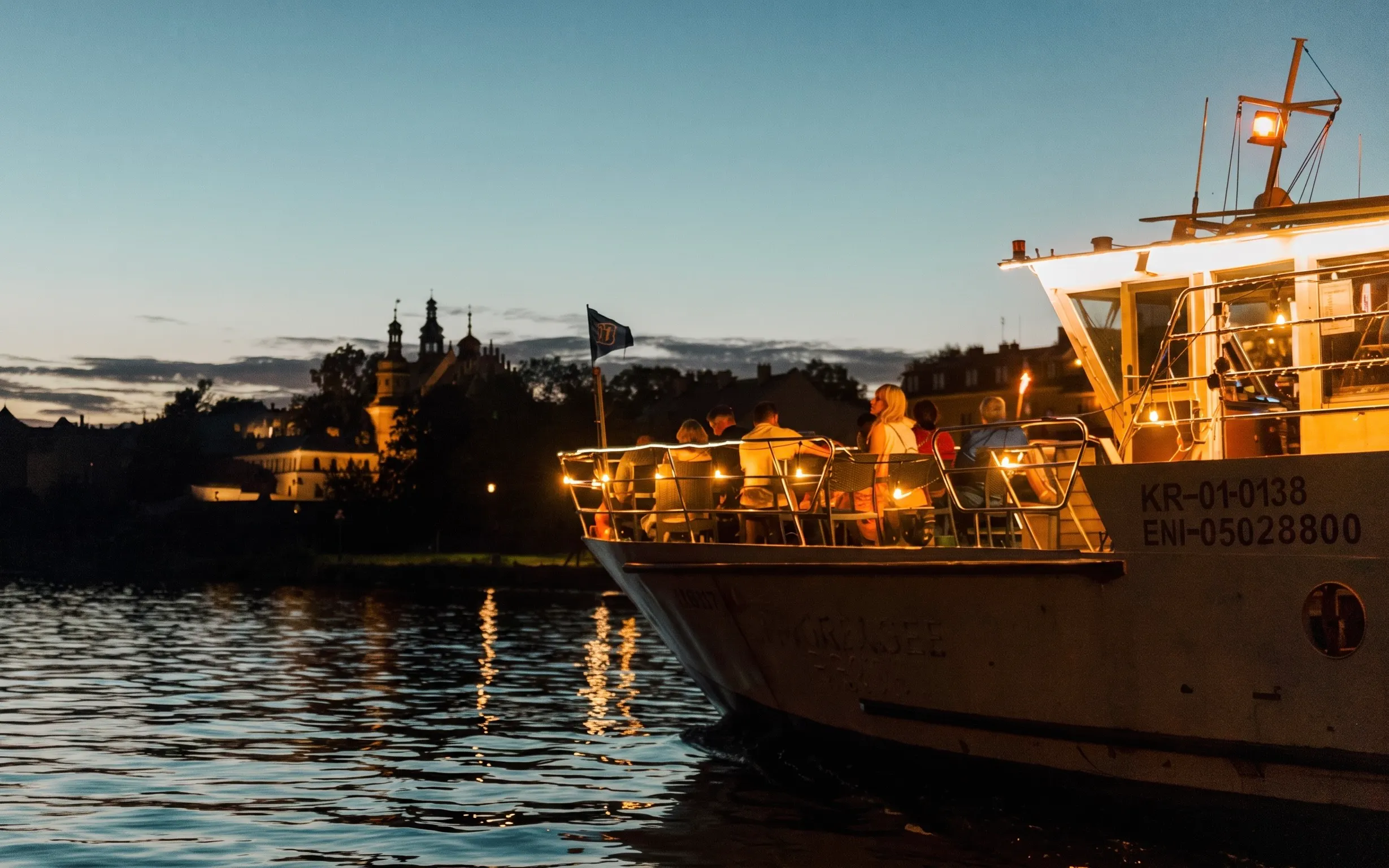Nighttime river cruise in Krakow with illuminated boat and city skyline.