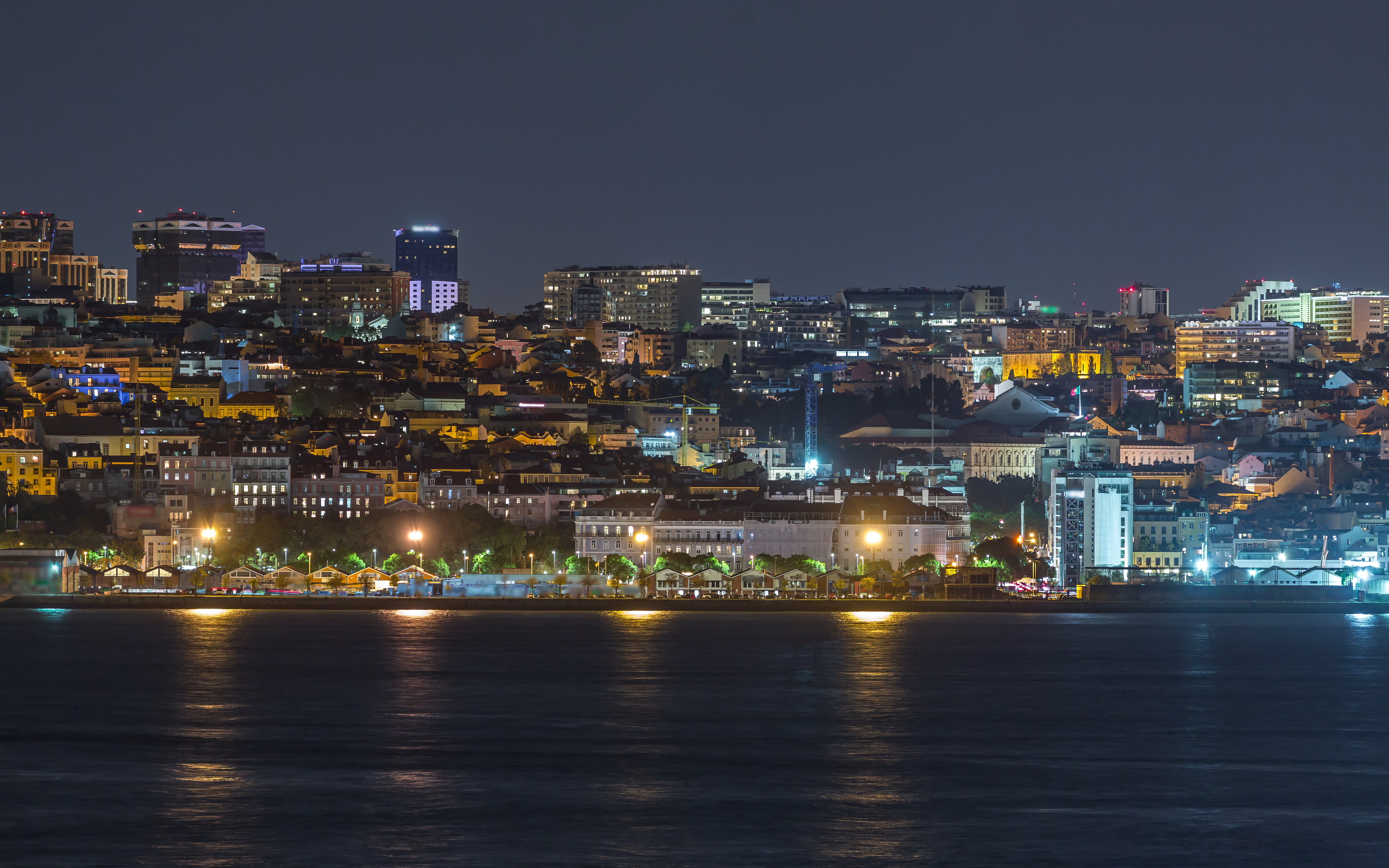 Lisbon skyline at night with illuminated Amoreiras towers reflecting on the water.