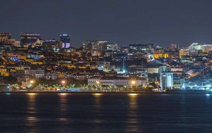 Lisbon skyline at night with illuminated Amoreiras towers reflecting on the water.