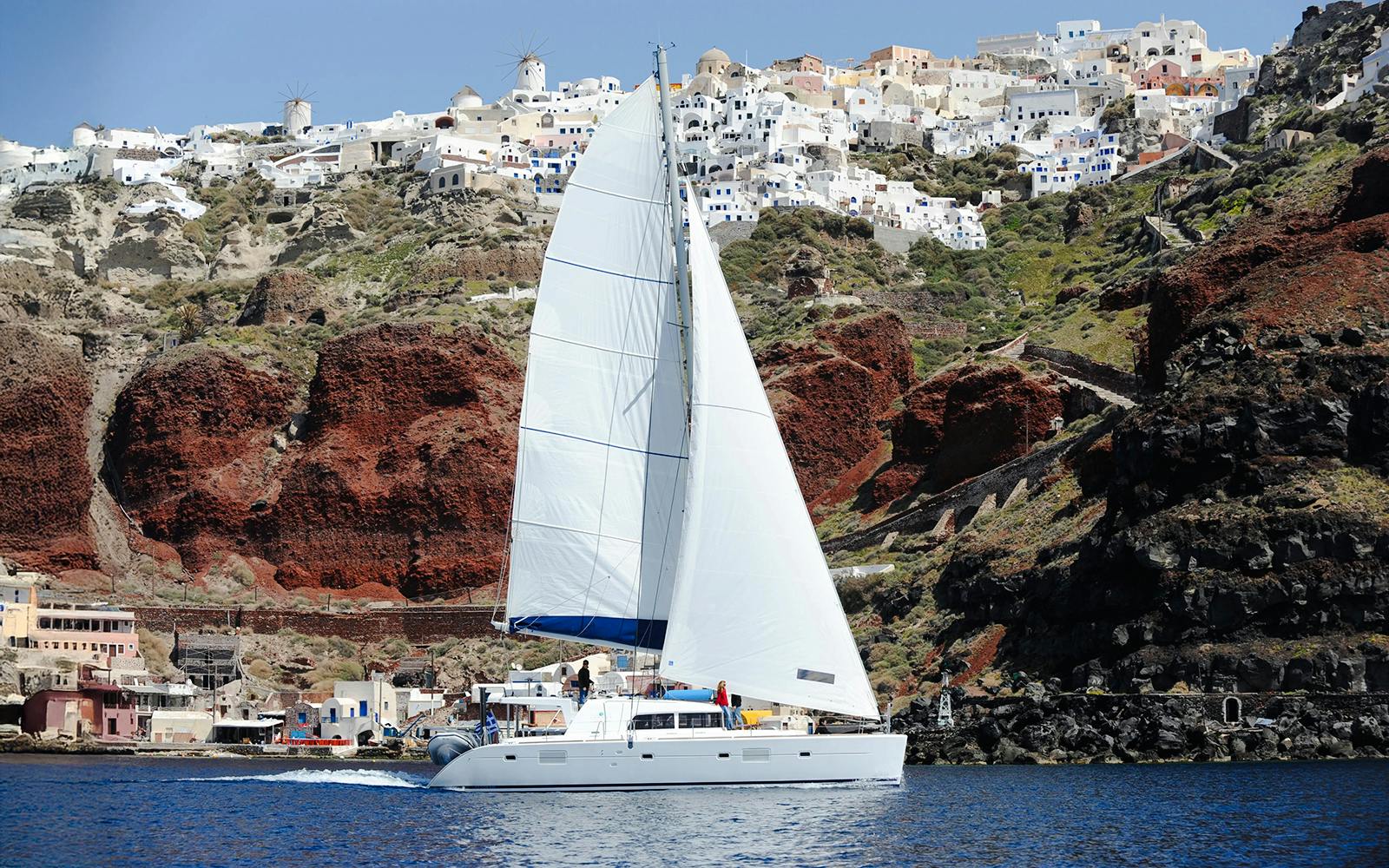 Luxury catamaran sailing near Red Beach cliffs in Santorini, Greece.