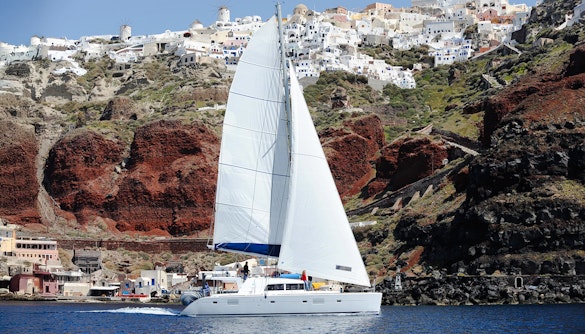 Luxury catamaran sailing near Red Beach cliffs in Santorini, Greece.