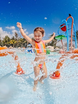 Little girl playing in waterpark splash zone on family vacation.