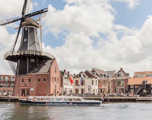 Canal cruise boat passing by a windmill and historic buildings in Haarlem.