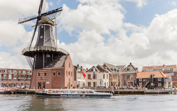 Canal cruise boat passing by a windmill and historic buildings in Haarlem.
