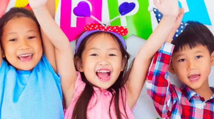 Children celebrating at KidZania with colorful balloons and a birthday banner.