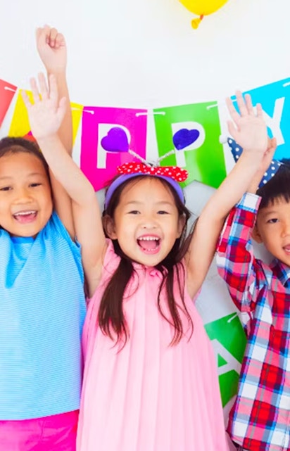 Children celebrating at KidZania with colorful balloons and a birthday banner.