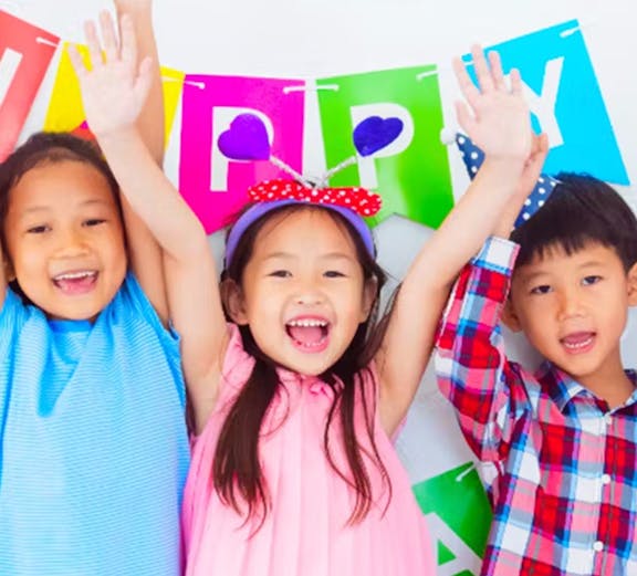 Children celebrating at KidZania with colorful balloons and a birthday banner.